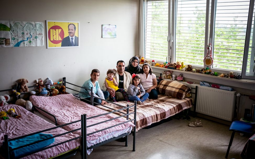 Bericht Flüchtlingskinder: Die Familie sitzt zusammen auf einem Bett in einer Flüchtlingskunterkunft