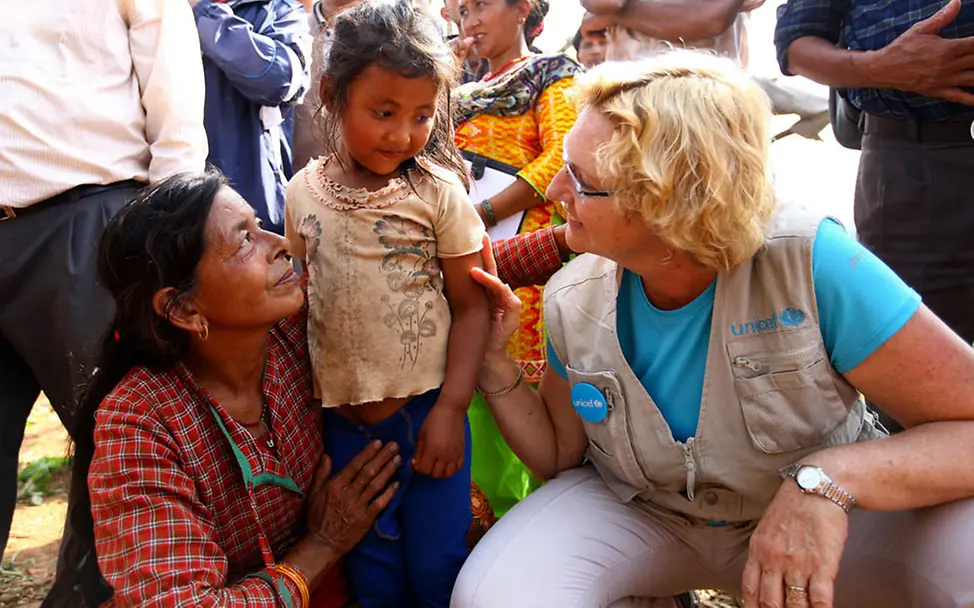 Nepal: UNICEF-Mitarbeiterin mit einer vom Erdbeben betroffenen Familie | © UNICEF/Panday Nepal Erdbeben: UNICEF-Mitarbeiterin mit einer betroffenen Familie. Sie kniet neben einem Mädchen und spricht mit ihm.