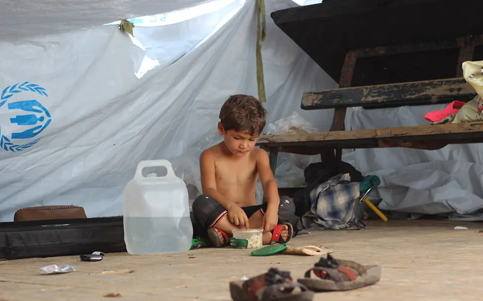 Ein kleiner Junge sitzt im provisorisch errichteten Zelt und isst. Er musste mit seiner Familie vor den neusten Anfriffen in Aleppo flüchten. | ©UNICEF/Khuder Al-Issa Ein kleiner Junge sitzt vor einem provisorischen Zelt. Er musste mit seiner Familie vor den neusten Angriffen flüchten.
