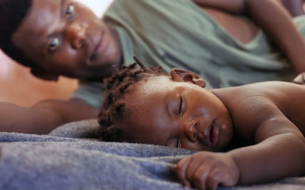 Dieser Vater liegt in einer Notunterkunft neben seinem schlafendem Baby. | © UNICEF/Moreno Gonzal Hurrikan Matthew: Dieser Vater liegt in einer Notunterkunft neben seinem schlafendem Baby.