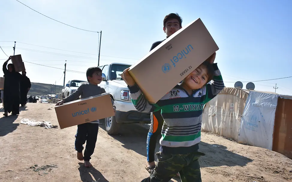 Die Hilfe im Irak kommt an! | © UNICEF/Hayder Drei Geschwister tragen in einem Flüchtlingslager im Irak Hilfspakete von UNICEF, die sie gerade erhalten haben.