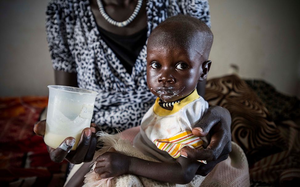 Die kleine Ayen aus dem Südsudan wird auf dem Schoß ihrer Mutter gefüttert.