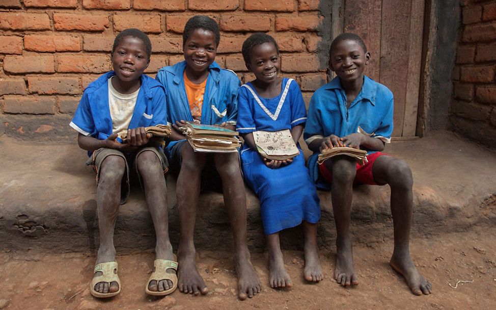 Malawi: Vier Kinder sitzen vor ihrem Haus mit ihren Schulbüchern