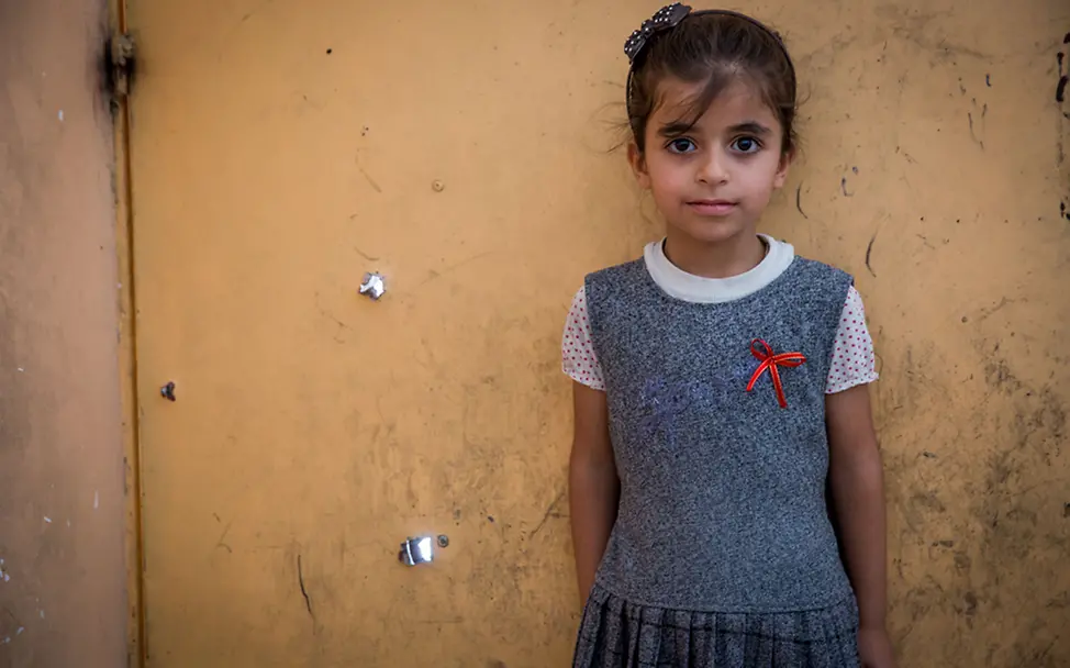 Abrar steht vor ihrer Hauswand, die mit Einschusslöchern übersäht ist. | © UNICEF/Anmar Irak, Mossul: Abrar steht vor ihrer Hauswand, die mit Einschusslöchern übersäht ist.