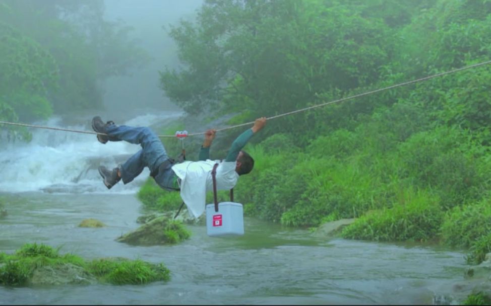 Indien: Ein Träger klettert an einem Seil über einen Fluss