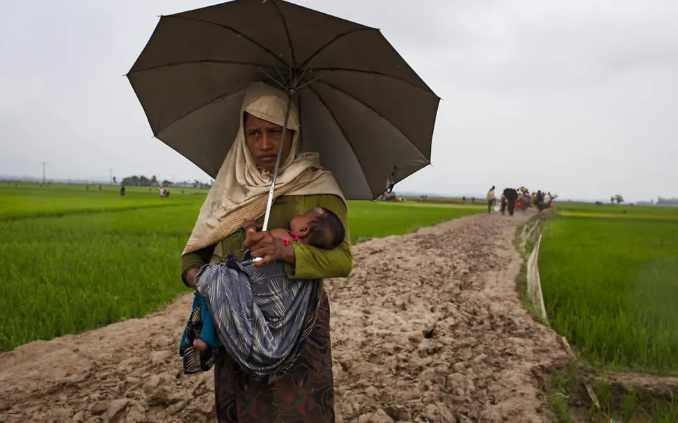 Eine Mutter trägt ihr Kind durch Reisfelder | © UNICEF/Brown Eine Mutter trägt ihr Kind im Regen durch Reisfelder