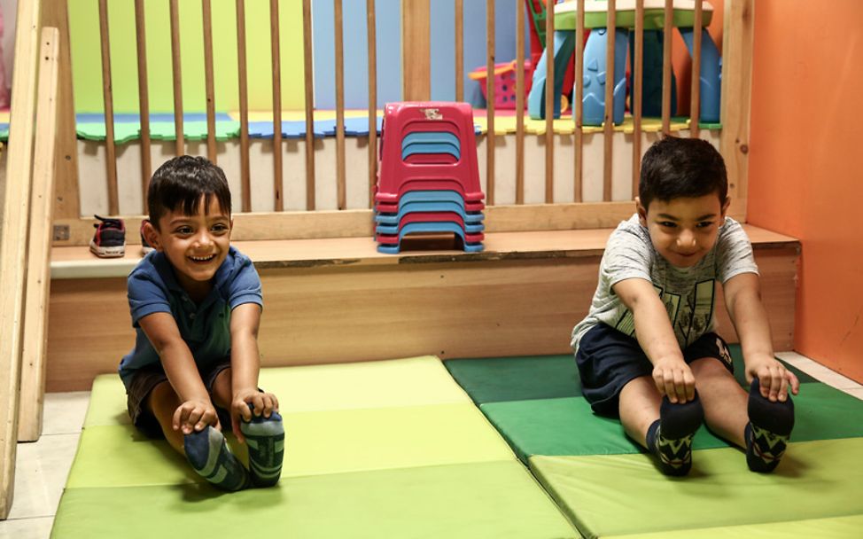 Zwei Kinder machen zusammen Dehnübungen und freuen sich.