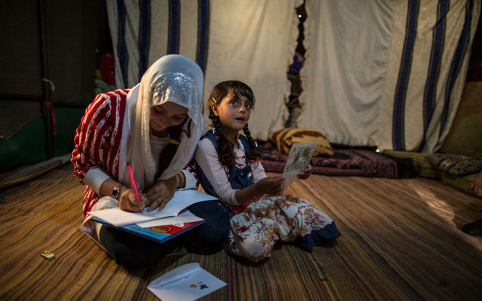 Zahra und ihre Schwester sitzen auf dem Boden und lesen und schreiben die Briefe.