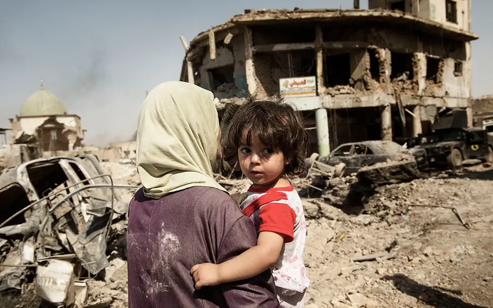 Mehr Hilfe für traumatisierte Kinder und Jugendliche! | © UNICEF/Romenzi Kind auf dem Arm einer Frau vor den Trümmern eines Hauses im Iraq