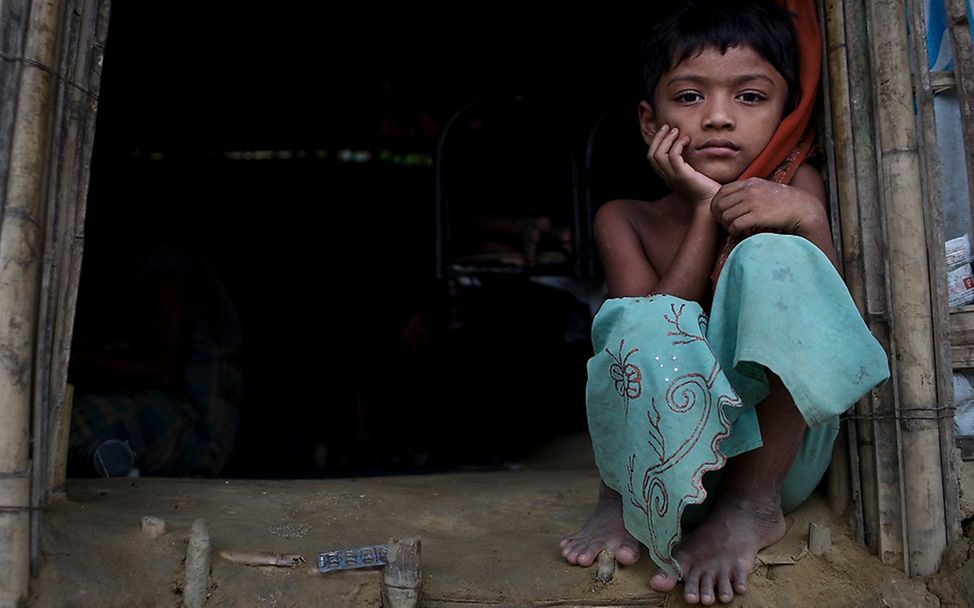 Ein Rohingya Mädchen sitzt in einem dunklen Hauseingang 