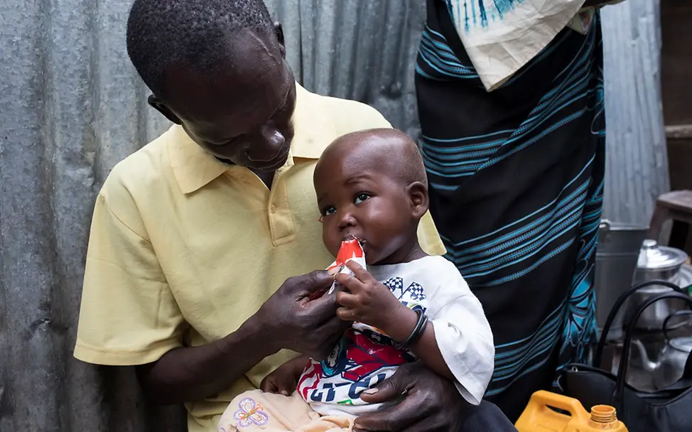 Erdnusspaste rettet Leben. | © UNICEF/Njiokiktjien Ein Vater füttert sein Kind mit Erdnusspaste.