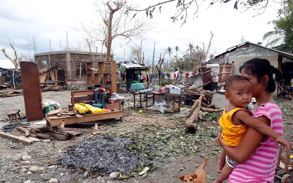 Eine Frau mit einem Kind auf dem Arm blickt auf die Zerstörung | © UNICEF/Maitem Philippinen Taifun Mangkhut: Mutter mit Kind neben zerstörtem Haus