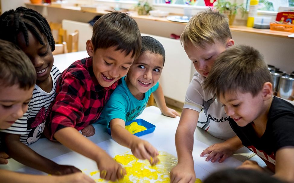 Sechs Jungen malen zusammen an einem Bild im Kindergarten