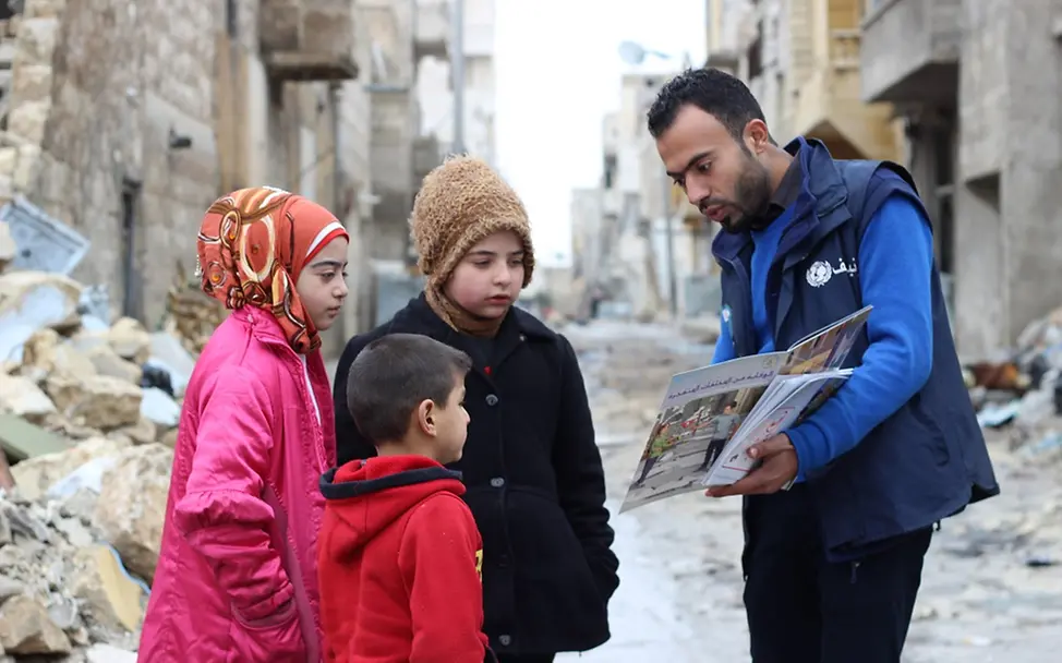 Mohammad ist ein Freiwilliger der Risiko-Aufklärungskampagne. Hier klärt er drei Kinder auf über z.B. Minengefahr in der Umgebung. | © UNICEF/Al-Issa Ein UNICEF Mitarbeiter klärt drei Kinder über die Risiken in der vom Krieg zerstörten Umgebung auf.