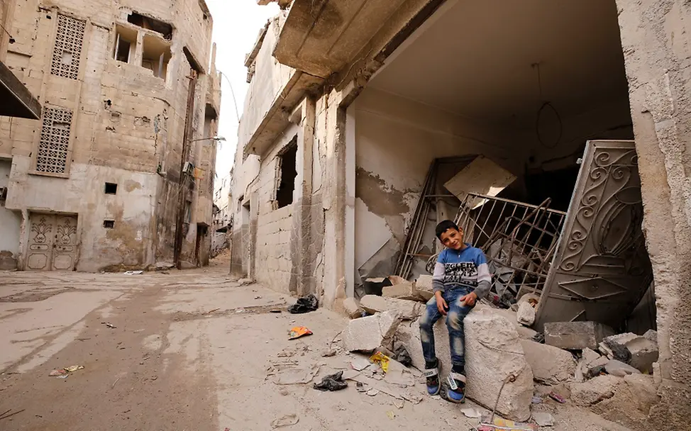 Ein Junge sitzt vor den Trümmern eines Hauses in Duma, Ostghouta. | © UNICEF/Sanadiki Ein Junge sitzt vor den Ruinen eines Wohnhauses.