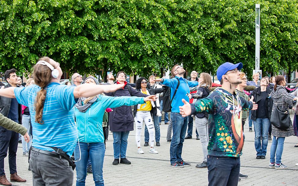 Mitwirkende beim Theater der 10.000 strecken ihre Arme aus.