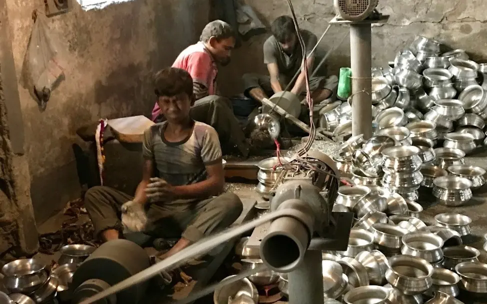 Die Jungen produzieren die Schüsseln ohne Augenschutz. | © UNICEF/Claudia Berger Kinderarbeit in Bangladesch: Ein Junge muss seine Augen wegen der Aluminiumsplitter zukneifen.