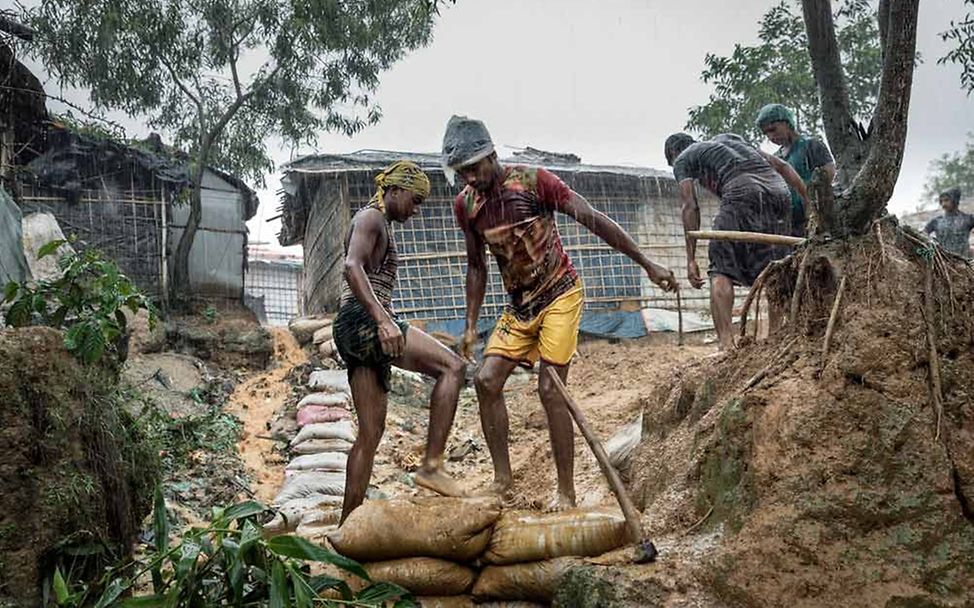 Monsun in Bangladesch 2019: Zwei Männer sichern einen Weg mit Sandsäcken