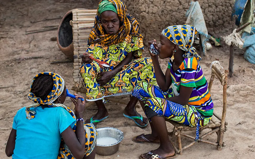 Gemeinsames Frühstück mit Mutter und Schwester. | © UNICEF/Dicko Mali: Fatoumata frühstückt mit ihrer Mutter und einer ihrer Schwestern Hirsebrei im Freien.
