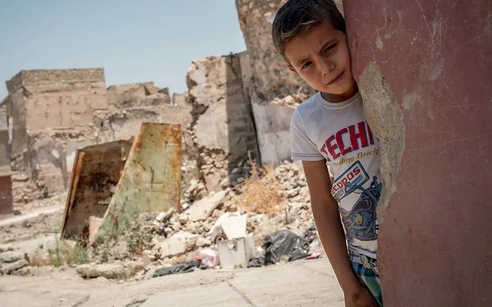 "Ich erinnere mich noch an das Geräusch der Granaten." - Ahmad aus dem Irak. | © UNICEF/Anmar Irak: Der Junge Ahmad steht angelehnt an einer Hausecke mit Einschussloch. Im Hintergrund Schutt und Geröll.