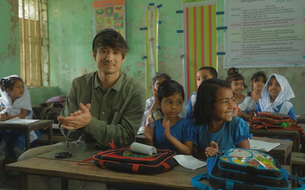 Bangladesch: Julien Bam sitzt mit zwei Mädchen in einer Schulbank.