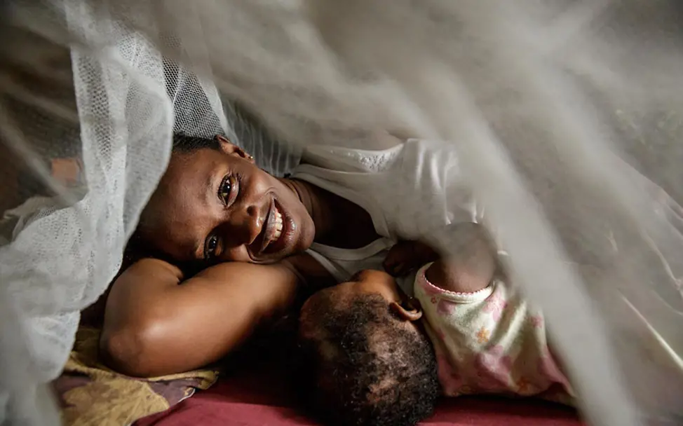 Ein Moskitonetz kann Leben retten. | © UNICEF/Asselin Issata und ihre vier Monate alte Tochter Davida liegen unter einem Moskitonetz.