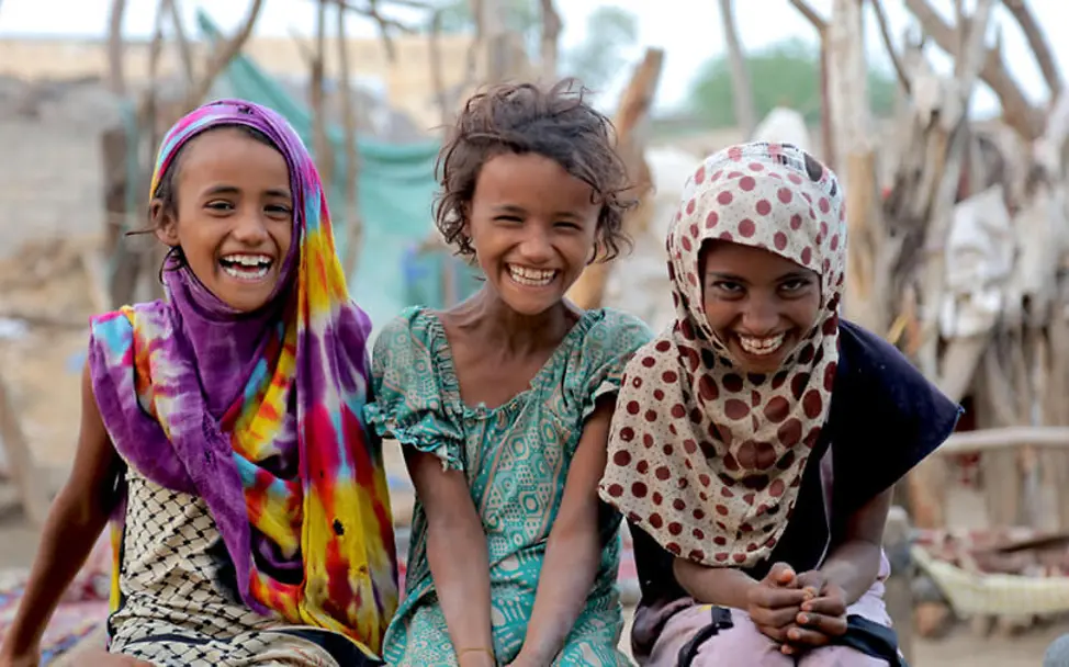 Alle Kinder haben ein Recht auf Leben. | © UNICEF/Almahbashi Wohlergehen von Kindern weltweit fördern: Drei Mädchen sitzen lachend auf einer Mauer.