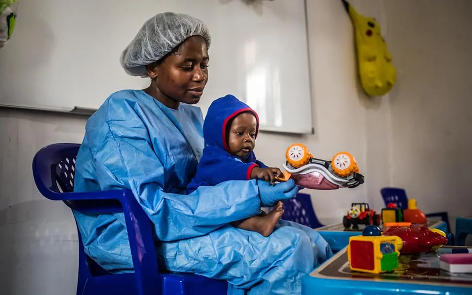 Ebola bekämpfen: Eine Ebolaüberlebende in Ebola-Schutzkleidung spielt mit einem Baby.