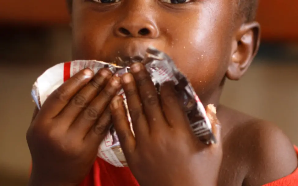 Erdnusspaste wird erfolgreich in der Therapie von mangelernährten Kindern eingesetzt. | © UNICEF/Asselin Ghana: Ein Junge isst genüsslich ein Päckchen Erdnusspaste.