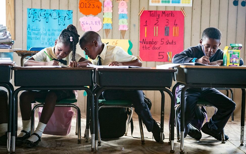 Auf der Insel Barabdu sitzen eine Schülerin und zwei Schüler an ihren Pulten im Klassenzimmer.