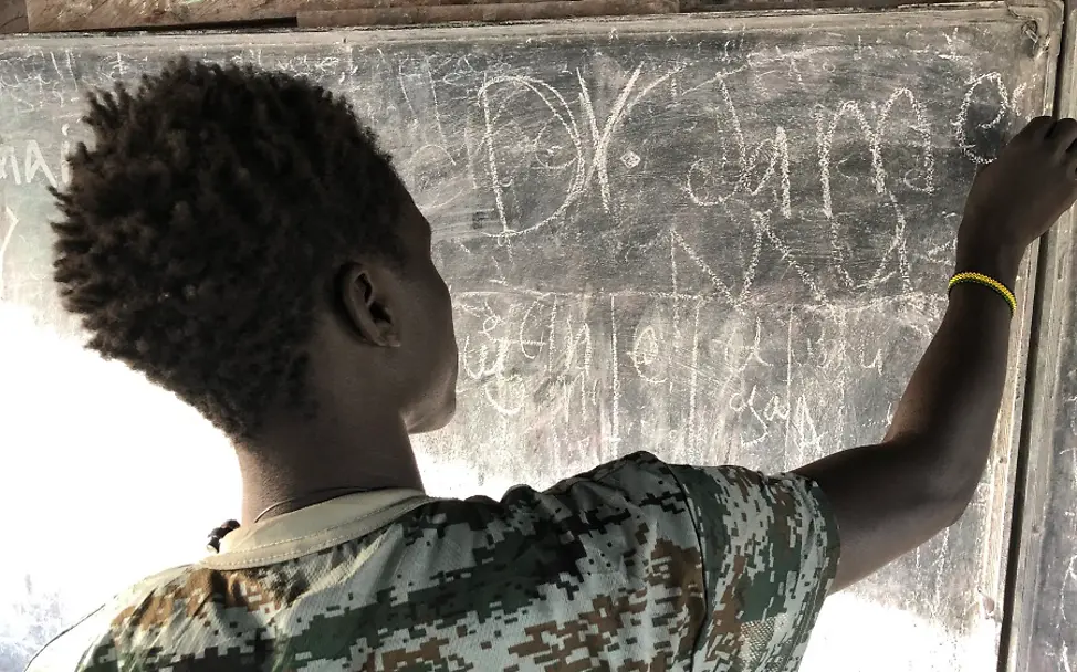 Südsudan: 'James' wurde als Kind von einer bewaffnete Gruppe entführt. | © UNICEF/Willemot Südsudan 2020: Ein Jugendlicher schreibt mit Kreide an eine Tafel