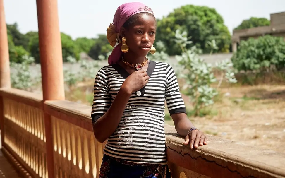 Guinea 2018: Fanta Traore (15). | © UNICEF/Brembati Guinea: Ein schwangeres Mädchen steht an einem Holzgeländer.