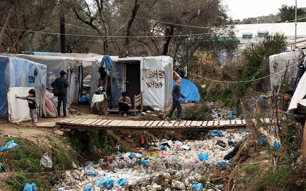 Flüchtlingslager Moria: Ein Kind läuft über eine Brücke, die über einen Bach aus Müll führt.