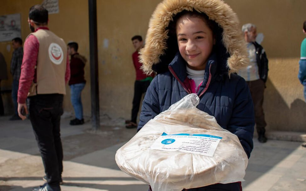 Syrien: Mädchen hält eine Tüte Brot mit einem Flyer zu Corona