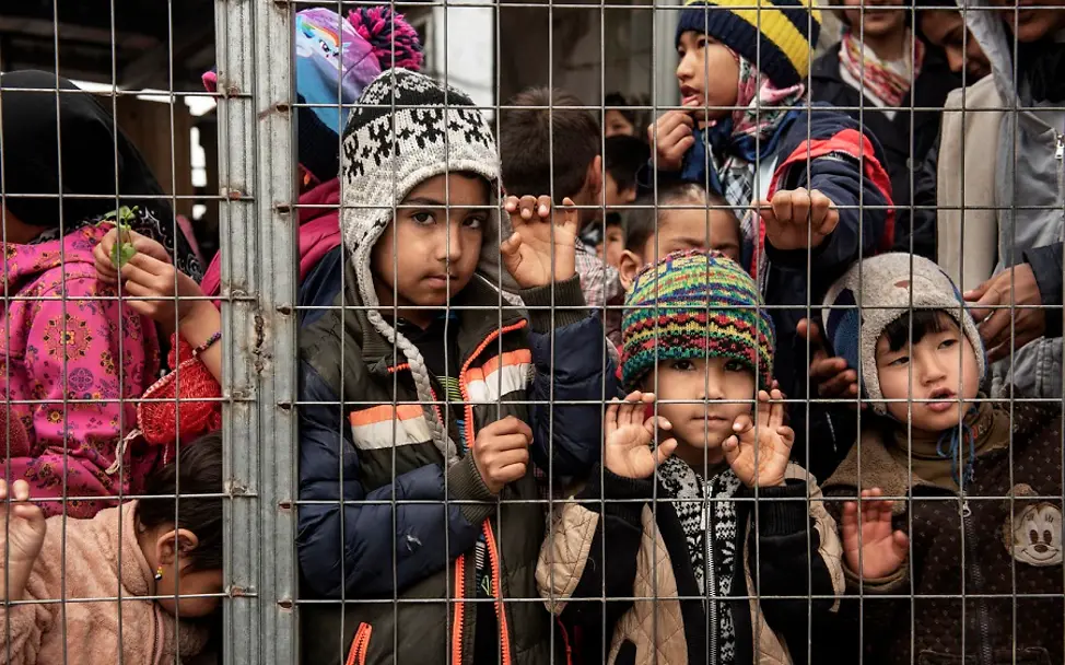 Das griechische Flüchtlingslager Moria im März 2020. | © UNICEF/Romenzi Kinder mit Wollmützen stehen hinter einem Gitter im Flüchtlingslager Moria.