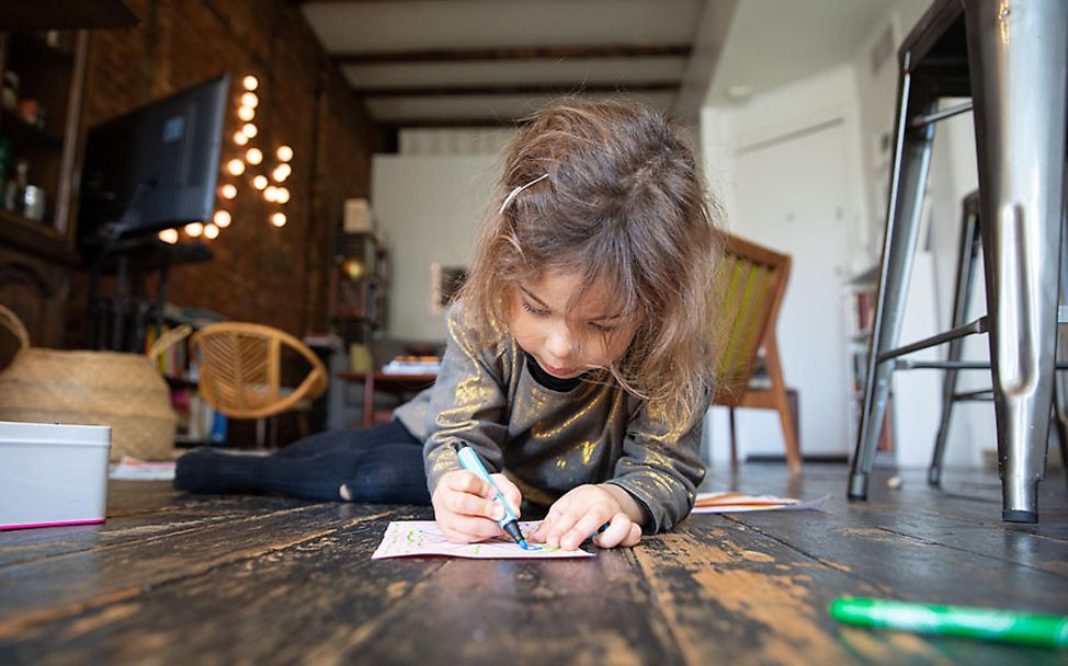 USA: Margot (4) sitzt auf dem Boden und malt ein Bild.