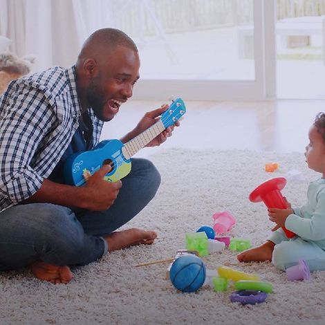 Babys und Musik: Vater spielt seiner Tochter etwas auf der Mini-Gitarre vor.