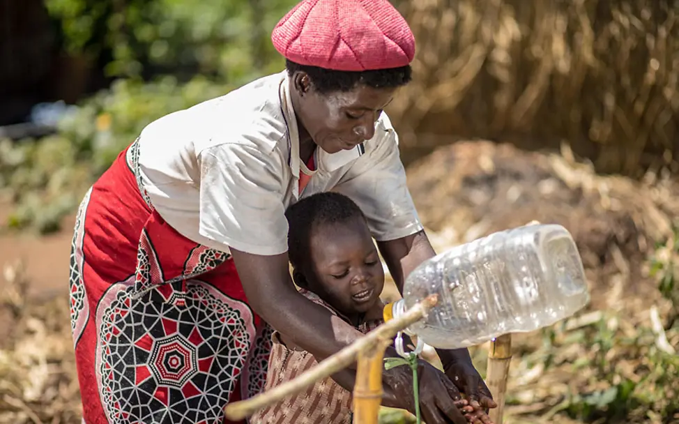 Esther bringt ihrem Enkel Isaac das Händewaschen bei. | © UNICEF Malawi: Esther bringt ihrem Sohn Isaac das Händewaschen bei.