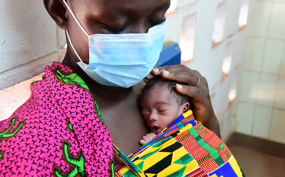 Elfenbeinküste 2020: Soro Sali kümmert sich um ein Baby ihrer verstorbenen Schwägerin. | © UNICEF/Frank Dejongh Schwangerschaft während Covid-19: Eine Frau mit Schutzmaske mit einem Neugeborenen auf der Brust