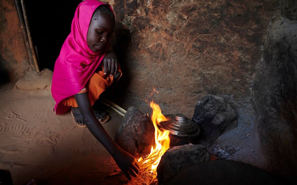 Flüchtlingslager Sudan: Mädchen hockt vor einer Feuerstelle.