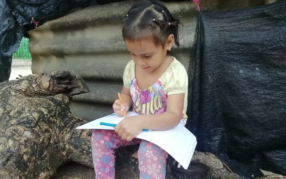 Kolumbien 2020. | © UNICEF/UNI331829 Covid-19: In Kolumbien sitzt ein Mädchen sitzt auf einem Baumstamm und schreibt in ein Schulheft.