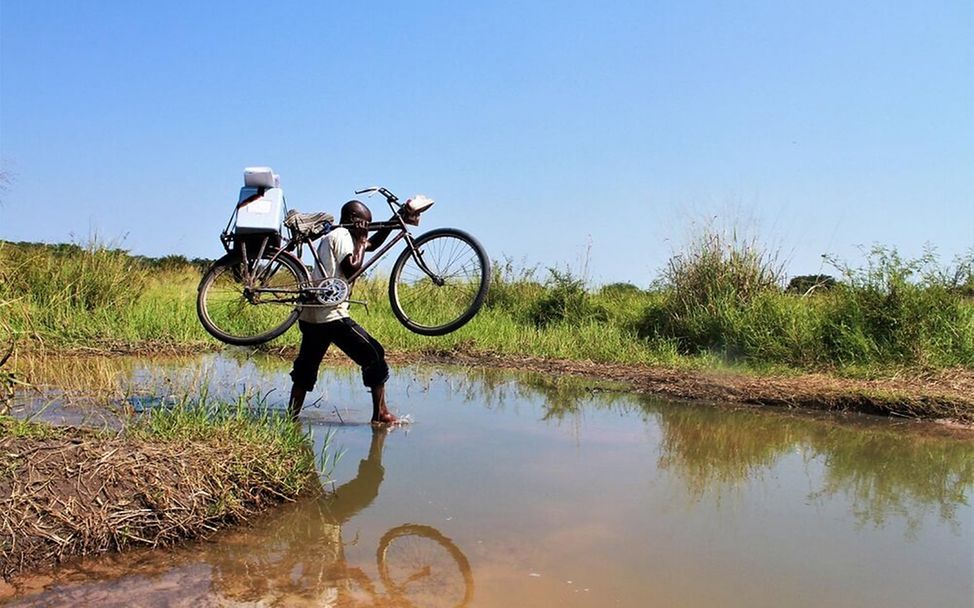 Kongo: Ein Impf-Helfer trägt sein Fahrrad über einen Fluss