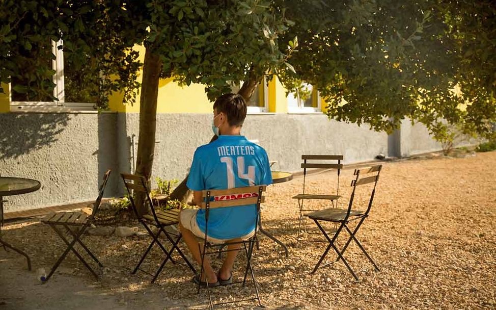 Bahnam sitzt im Hof der Notunterkunft Tapuat auf einem Stuhl unter einem Baum.