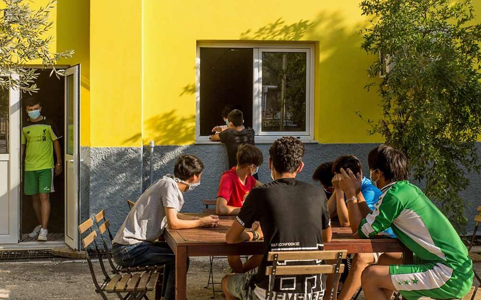 Mehrere geflüchtete Jugendliche sitzen zusammen im Hof des Kinderzentrums an einem Tisch.