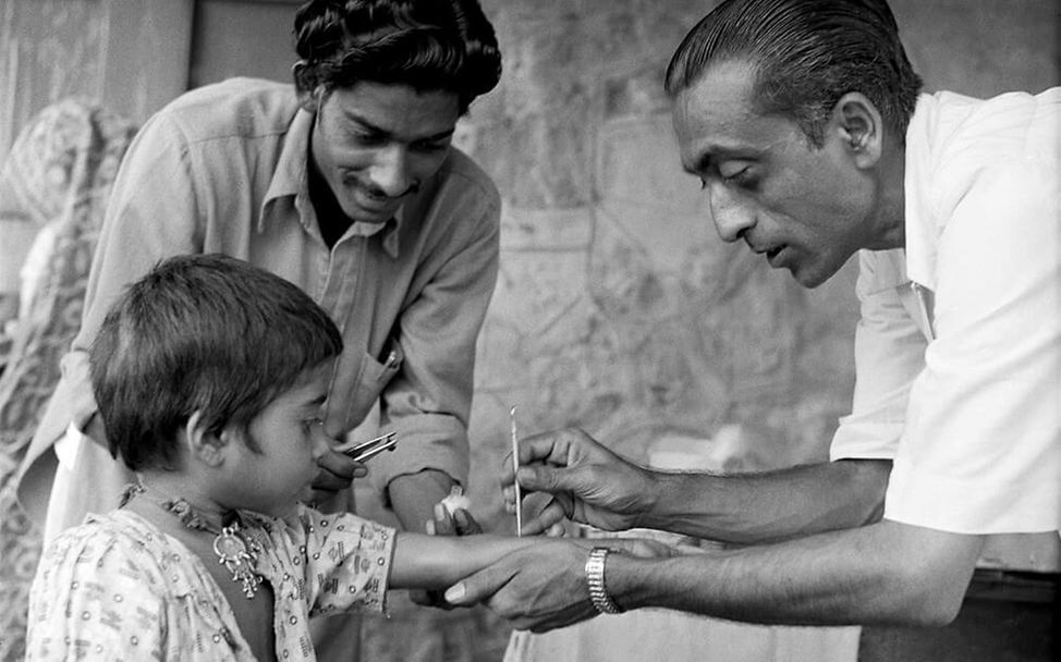 Indien, 1961: Ein Mädchen schaut gespannt zu, wie ein UNICEF-Gesundheitshelfer es gegen Pocken impft.