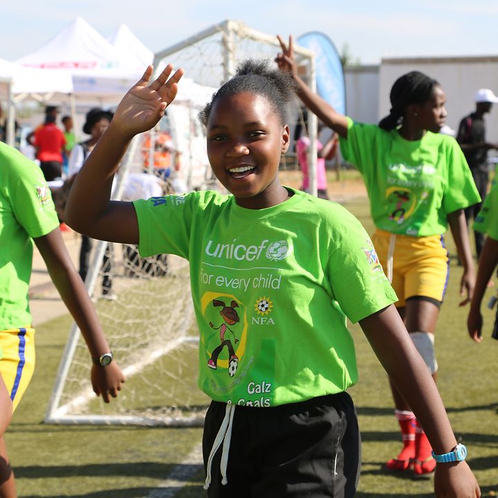 Ein Mädchen aus einem Fußball-Team winkt fröhlich in die Kamera. Sie trägt ein UNICEF-Trikot.