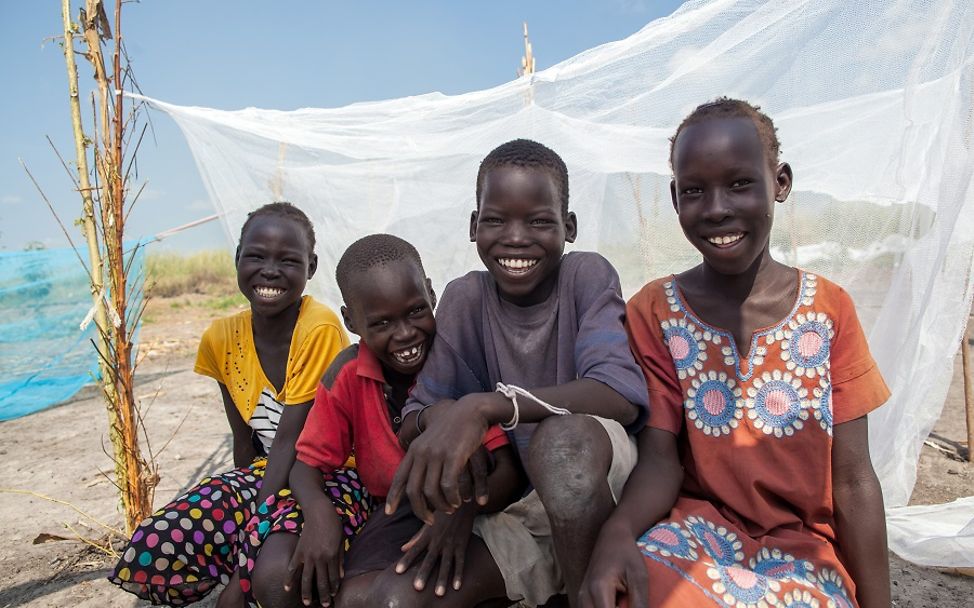 Südsudan 2020: Vier Kinder sitzen lachend vor einem von UNICEF bereitgestellten Moskitonetz