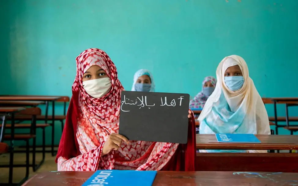Covid-19: Schule während Covid-19 | © UNICEF/Pouget Covid-19: Zwei Mädchen aus Mauretanien mit Schild "Ich liebe Schule" auf Arabisch