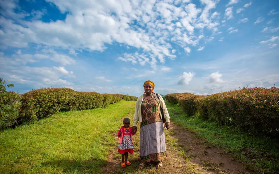 Chantal musste ihre Tochter lange Zeit während zur Arbeit mitnehmen. | © UNICEF/Rudakubana Ruanda: Mutter und Kind stehen auf einem Feld.