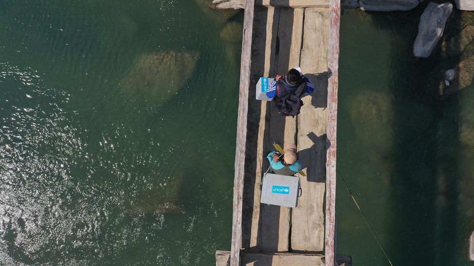 Ein Drohenfoto zeigt den Transport von Vakzinen über eine schmale Brücke.